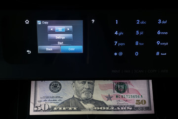 Black multifunction printer with touch screen display makes copy of 50 dollar bill in the dark. Printing money at home.