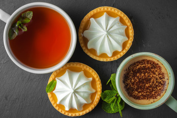 Lemon tart with mint leaves, a cup of tea and a cup of cappuccino with chocolate topping