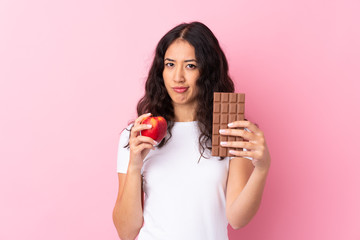 Spanish Chinese woman over isolated pink background taking a chocolate tablet in one hand and an...