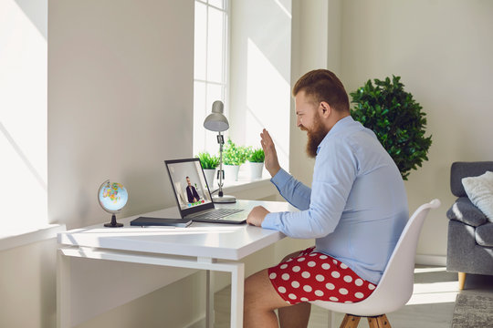 Online work at home. Funny man in red shorts communicates using laptop sitting at the table at home.