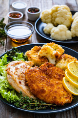 Pork chops with fried cauliflower and vegetable salad on wooden background