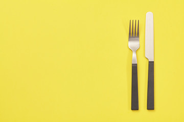 Black knife and fork on yellow background. Top view