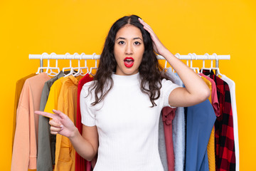 Mixed race woman in a clothing store surprised and pointing finger to the side