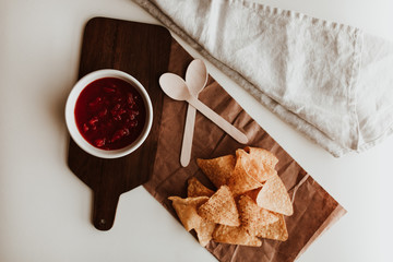 Tortilla chips on recycled paper with tomato sauce and wooden spoons and linen napkin