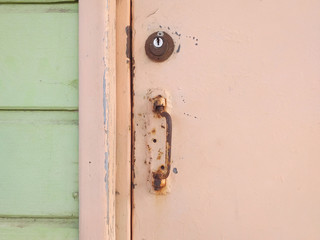 Close-up of pale pink rusty Caribbean house door, door handle, lock and light green wooden facade....
