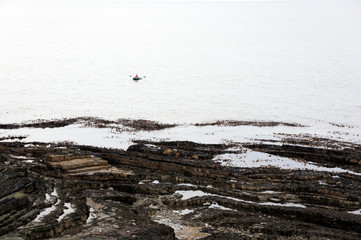 A lonely man in a boat near the layered shore of the Irish Sea.