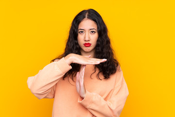 Spanish Chinese woman over isolated yellow background making time out gesture