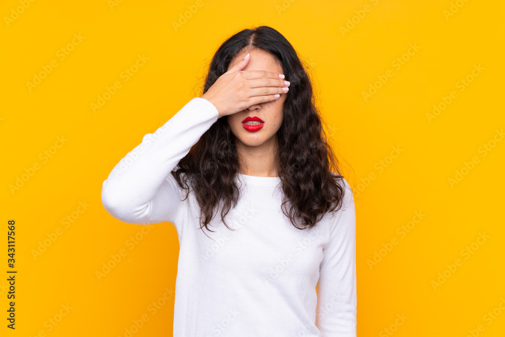 Wall mural Mixed race woman over isolated yellow background covering eyes by hands