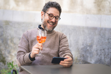 A middle-aged man toasts with friends at a virtual party on the terrace in a video call with a...