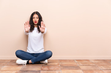 Young woman sitting on the floor making stop gesture and disappointed