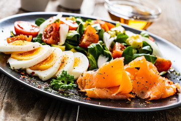 Salmon salad - smoked salmon, boiled eggs and vegetables on wooden background
