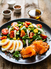 Salmon salad - smoked salmon, boiled eggs and vegetables on wooden background
