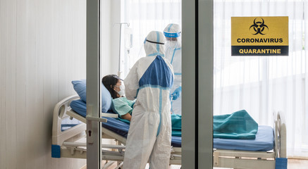 Two asian doctor wear PPE suit with N95 mask and face shield, treat coronavirus infected patient in negative pressure room, label with quarantine alert area sign. Coronavirus and covid19 concept.