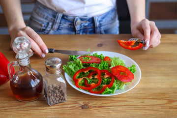 Women's hands hold a knife and fork near the salad, a woman eats a healthy salad of vegetables