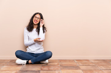 Young woman sitting on the floor with glasses and happy