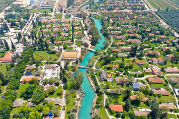 Fototapeta na wymiar Aerial image of Kibbutz Nir David with Amal river channel turquoise water dividing east and west side riverside houses and palm trees, Israel.