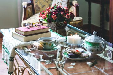 Obraz na płótnie Canvas Glass living room table with a cup of tea, cookies, candles, books and reading glasses 