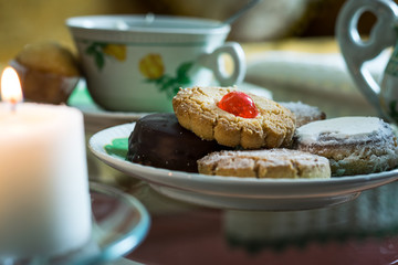 Plate of cookies next to candles and cup of tea in background on glass table
