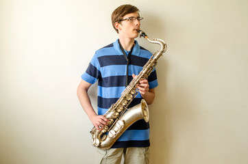 Fototapeta na wymiar Young saxophonist plays tenor saxophone in a striped blue shirt on a white background 