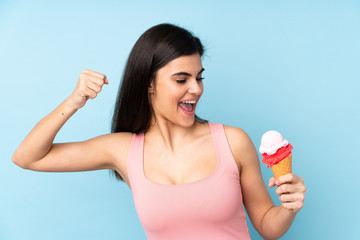 Young woman holding a cornet ice cream over isolated blue background celebrating a victory