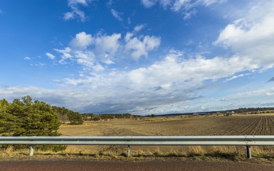 Beautiful spring day and the view from the car.
Gorgeous landscape with fields, forest trees and blue sky with white clouds. Sweden.