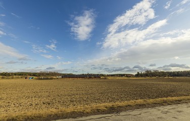 Fototapeta premium Beautiful nature landscape view on spring day. Plowed field merging with blue sky and white clouds. 