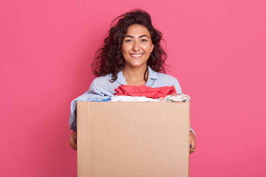Closeup portrait of happy caucasian brunette woman holding carton box with donation, adorable female posing isolated over pink studio background, dark haired girl looking directly at camera.