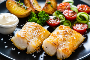 Fish dish - fried cod fillet with vegetables on wooden table
