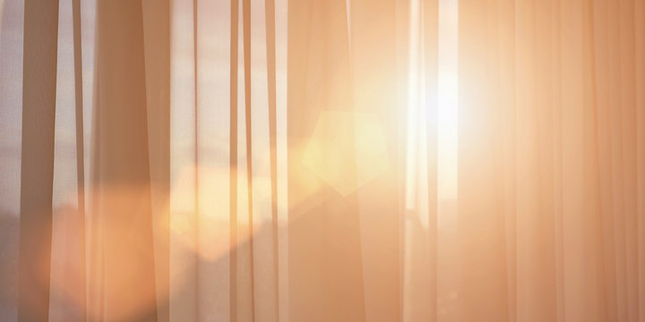 ray of sun lighting through transparent curtain on window into bedroom