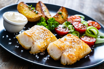 Fish dish - fried cod fillet with vegetables on wooden table

