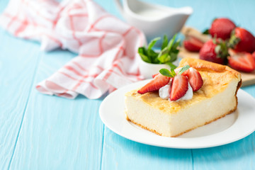 Cottage cheese casserole or pudding with fresh summer strawberries on blue wooden table, copy space for text or design elements. Breakfast cheese cake