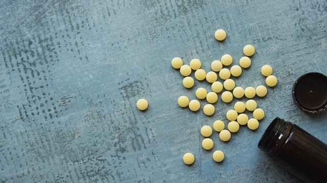 yellow round tablets or pills vitamins flat lay on blue stone concrete table with black plastic bottle, top down view, horizontal stock photo image still life background with copy space