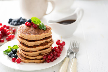 Whole wheat pancakes with berries on white table, healthy breakfast stack of pancakes. Copy space on white background