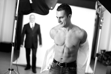 Fototapeta na wymiar Modello si toglie la camicia in studio , sullo sfondo uno studio fotografico con un uomo in abito