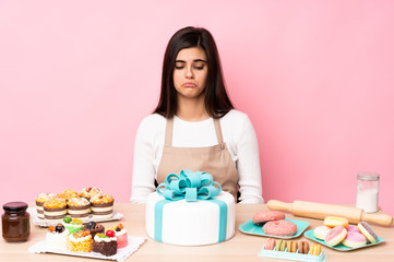 Obraz na płótnie Canvas Pastry chef with a big cake in a table over isolated pink background with sad and depressed expression