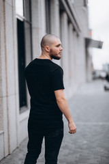Fototapeta premium portrait of a bald handsome bearded man in a black t-shirt on the street, who looks away