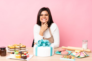 Obraz na płótnie Canvas Pastry chef with a big cake in a table over isolated pink background with glasses and smiling