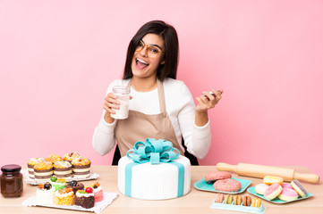 Pastry chef with a big cake in a table over isolated pink background