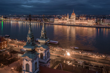 Fototapeta premium Budapest, Hungary - Aerial view of the Saint Anne Parish Church at Batthyany Square at dusk with illuminated Hungarian Parliament building and cloudy dark blue sky at background