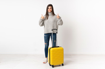 A full length body of a traveler woman with a suitcase over isolated white wall giving a thumbs up gesture