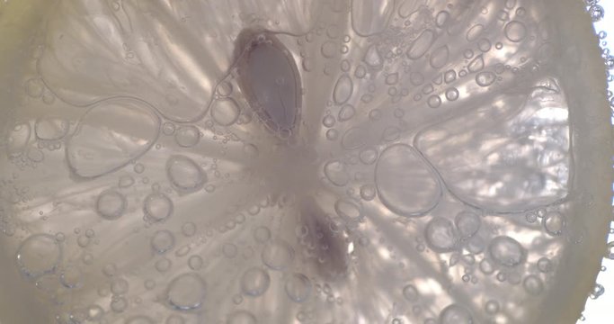 Slice of lemon under water with air bubbles.