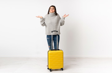 A full length body of a traveler woman with a suitcase over isolated white wall having doubts with confuse face expression