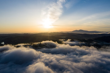 Fototapeta na wymiar Sunrise illuminates the marine layer covering hills and valleys in California's Bay Area. The foggy marine layer is a climatic phenomenon that is an almost daily occurrence in this region.