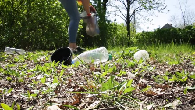 A young woman collects a plastic in the forest. Activist with black garbage bag in nature in the park. Concept about environmental conservation pollution problems. Ecology