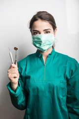 dentista con mascherina verde cuffietta verde e camice verde che mostra i suoi strumenti di lavoro...