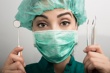 dentista con mascherina verde cuffietta verde e camice verde che mostra i suoi strumenti di lavoro...