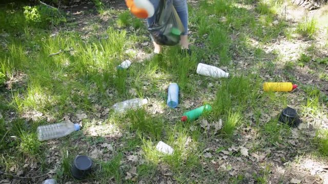 A young woman collects a plastic in the forest. Activist with black garbage bag in nature in the park. Concept about environmental conservation pollution problems. Ecology