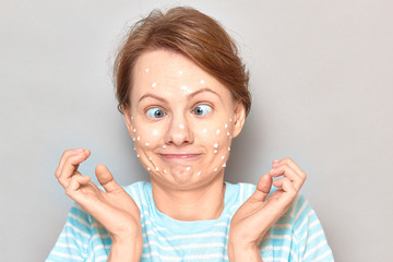 Portrait of funny goofy cheerful girl with drops of face cream on skin