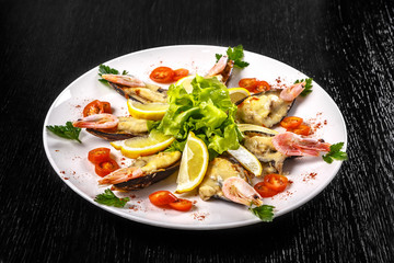 Shrimps, tomatoes and lemon are beautifully laid out on a dish on a black background.