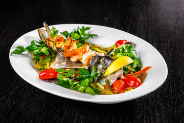 The head of the fish, mussels, greens and prawns are on a white plate